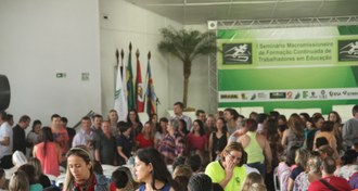 Pessoas em pé em um grande salão, ao fundo o cartaz do I Seminário, ocorrido em 2014