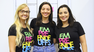 Foto com três mulheres sorrindo, em plano americano. Elas estão com camisetas pretas, escrito "Empreende UFFS" em letras coloridas