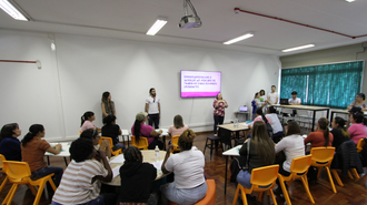 Foto com várias mulheres de costas, sentadas em uma sala, olhado para uma mulher falando