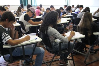 Em plano aberto, foto mostra estudantes fazendo provas em uma sala de aula