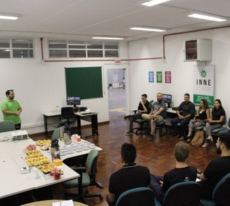 Foto em plano aberto, com o professor à frente e grupo sentado em cadeiras dispostas em C