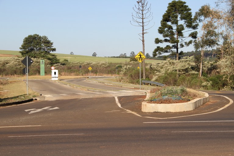 Foto mostra a entrada da UFFS - Campus Chapecó, no entroncamento com a rodovia. Há árvores ao redor, uma guarita ao centro e, na mesma direção, mas mais longe, um totem de identificação da UFFS