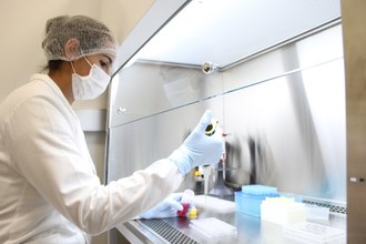 Mulher paramentada com luvas, touca, máscara e jaleco, trabalhando em laboratório