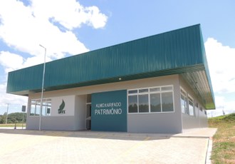 Fotografia mostra a estrutura física do Galpão de Almoxarifado e Patrimônio. A foto destaca a frente e uma lateral da obra. Ao lado esquerdo da porta de entrada está ilustrada a identidade visual da UFFS e, ao lado direito, as palavras "Almoxarifado e Patrimônio".