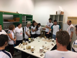 Os estudantes formam um círculo ao redor de mesas onde estão expostos materiais relacionados à Aquicultura.