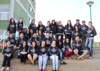 Na imagem, um grupo de acadêmicos sentados em uma escadaria, ao fundo o bloco de salas de aula.