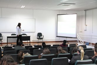 Na imagem a mestranda Leide permanece em pé a frente da plateia e apresenta o trabalho apontando para informações projetadas em telão. Foto: Éliton Novais/Ascom-LS/UFFS