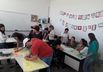 Na imagem três grupos de professores desenvolvem atividades utilizando cartolinas.