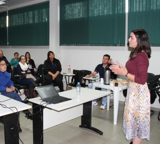 Na foto a palestrante, Pricila Mortiz, está em pé falando para a plateia que acompanha a apresentação.