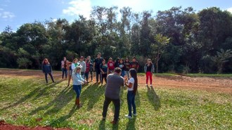 Na foto um grupo de pessoas está em pé observando a apresentação do docente.