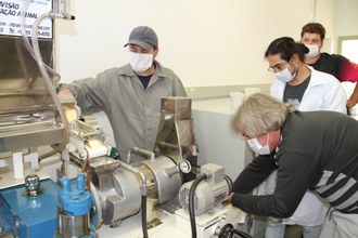 Foto mostra quatro pessoas observando e manuseando a extrusora.