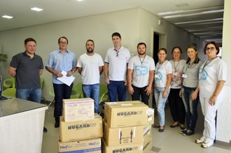 Na foto, a frente, caixas de papelão com os materiais doados e, ao fundo, pessoas.