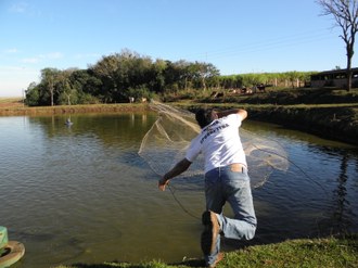 Na imagem um homem lança uma rede de pesca em um lago.